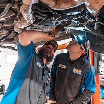 Mechanics inspecting vehicle underside in garage